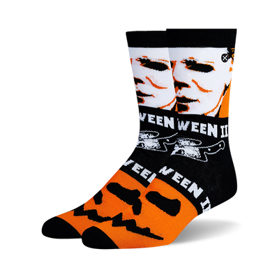 Pair of crew socks angled left, black and orange. Design features Michael Myers face, Halloween text, knives, and jack-o'-lanterns.