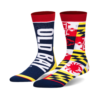 Pair of Old Bay Split crew socks. One sock displays the 'Old Bay' logo in white against a navy blue background. The other sock features a patchwork design of the Maryland state flag, incorporating red, white, yellow, and a crab.