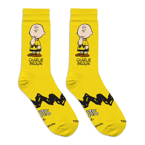 Flat lay of two bright yellow crew socks showing a Charlie Brown graphic, zigzag stripe, and Peanuts logo on the soles.