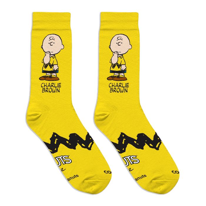 Flat lay of two bright yellow crew socks showing a Charlie Brown graphic, zigzag stripe, and Peanuts logo on the soles.