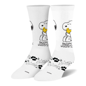 White crew socks showing Snoopy hugging a yellow Woodstock, with black paw prints and swirling line patterns on the foot.