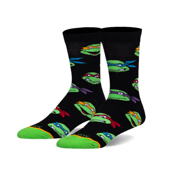 A pair of black crew socks with a repeating pattern of green turtle heads wearing red, blue, orange, and purple masks. Green toe and heel.