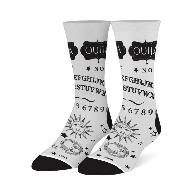 White crew socks with a black Ouija board design, featuring the alphabet, numbers, stars, and vintage sun and moon faces.