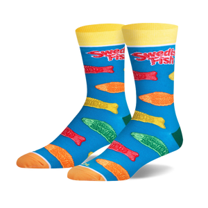 Pair of crew socks with a teal background. Features colorful Swedish Fish candy printed on them, and yellow cuffs with 'Swedish Fish' logo.