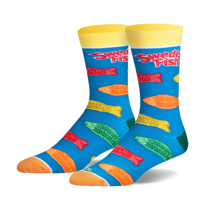 Pair of crew socks with a teal background. Features colorful Swedish Fish candy printed on them, and yellow cuffs with 'Swedish Fish' logo.