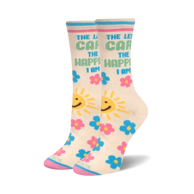 A pair of cream crew socks with "The Less I Care, The Happier I Am" text, smiling yellow suns, and pink and blue flowers. Pink toes are visible.