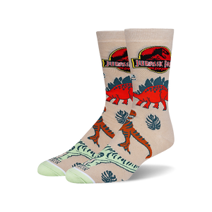 Tan crew socks with a Jurassic Park theme.  Features red and orange dinosaurs, tropical leaves, and the Jurassic Park logo.