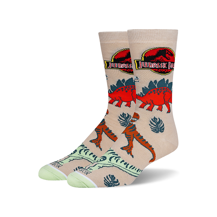 Tan crew socks with a Jurassic Park theme.  Features red and orange dinosaurs, tropical leaves, and the Jurassic Park logo.