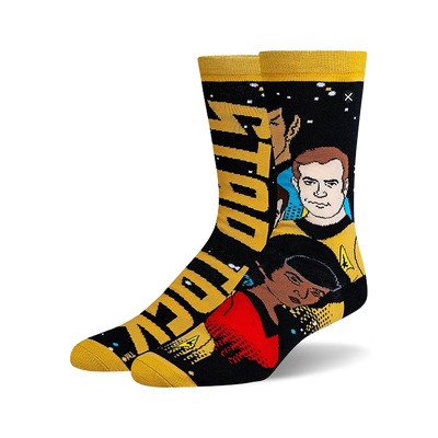 Two Star Trek crew socks standing upright. One black with white 'STAR TREK' logo, the other black with Kirk, Spock, and Uhura. Both have gold cuffs and toes.
