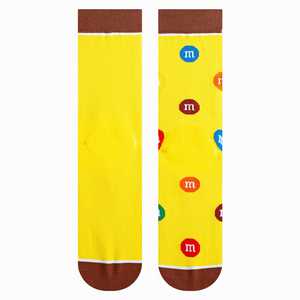 Close-up shot highlighting the sock's texture and details. Yellow background with scattered M&Ms and a brown cuff.