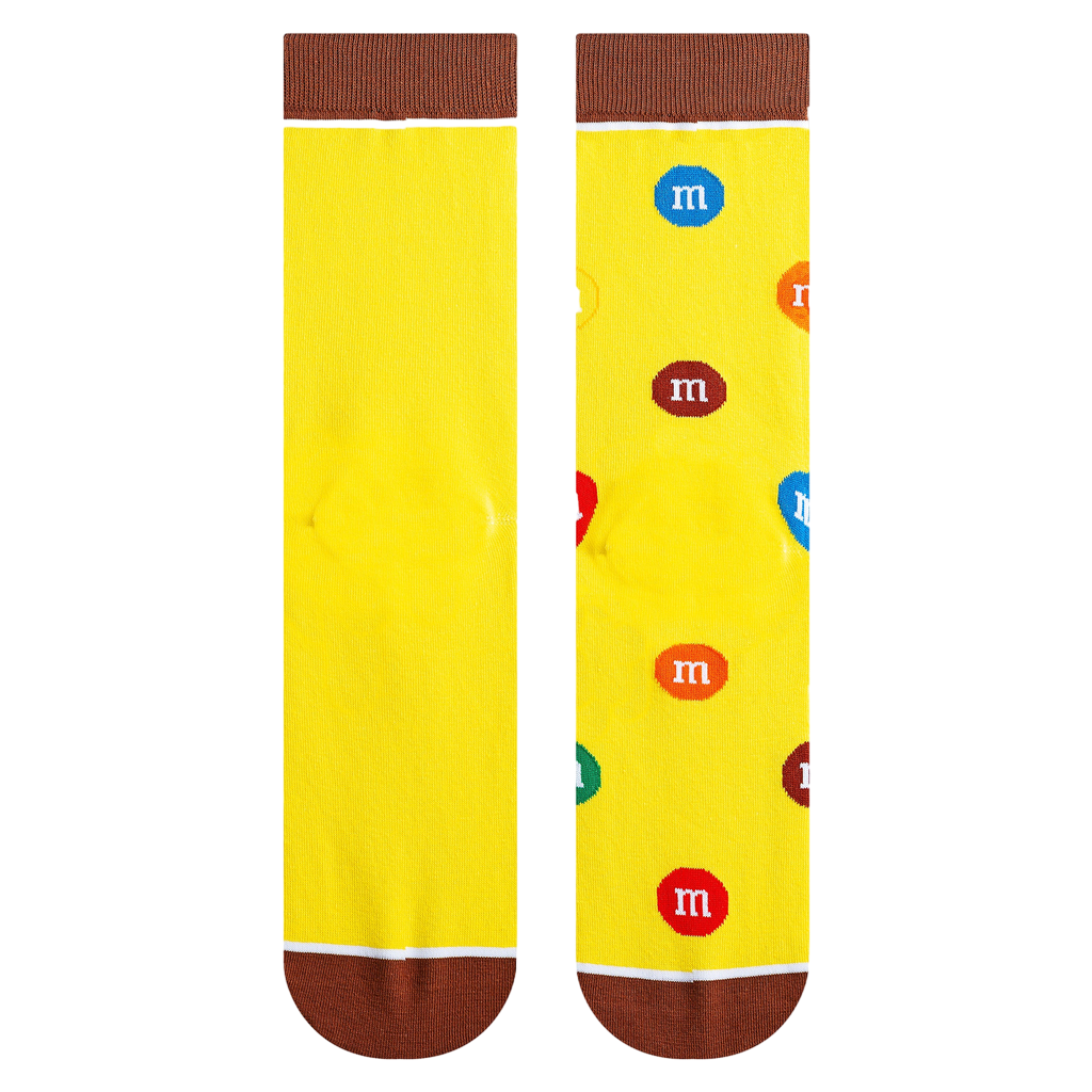 Close-up shot highlighting the sock's texture and details. Yellow background with scattered M&Ms and a brown cuff.