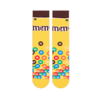 Flat lay of yellow crew socks showing a brown cuff, the M&M's logo on the calf, and colorful M&M candies piled at the toe.