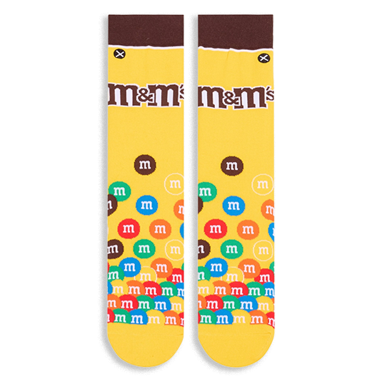 Flat lay of yellow crew socks showing a brown cuff, the M&M's logo on the calf, and colorful M&M candies piled at the toe.