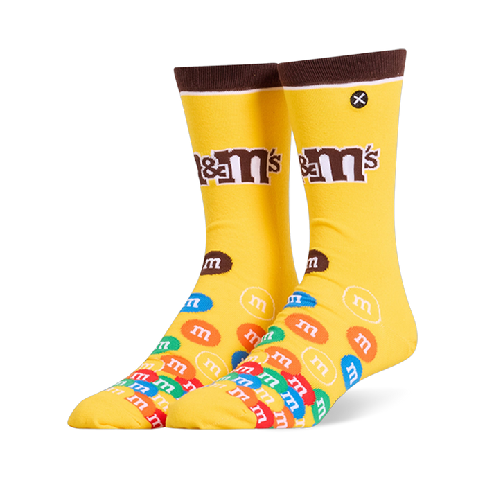 Bright yellow crew socks featuring a brown cuff, the M&M's logo on the leg, and a colorful pile of M&M candies on the foot.
