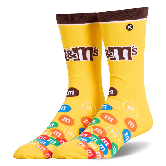 Bright yellow crew socks featuring a brown cuff, the M&M's logo on the leg, and a colorful pile of M&M candies on the foot.