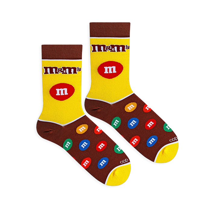 Flat lay of yellow and brown M&M's socks showing the classic logo, a large red candy on the leg, and a colorful candy foot.