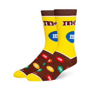 Yellow and brown M&M's crew socks with the classic logo on the leg and a pattern of colorful candy pieces on the dark foot.