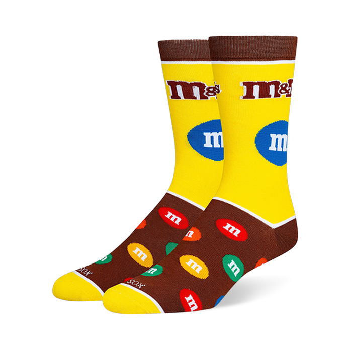 Yellow and brown M&M's crew socks with the classic logo on the leg and a pattern of colorful candy pieces on the dark foot.