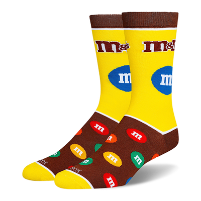 Yellow and brown M&M's crew socks with the classic logo on the leg and a pattern of colorful candy pieces on the dark foot.
