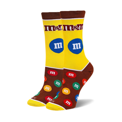 Pair of crew socks with bright yellow shaft, chocolate brown foot, M&M's logo and scattered colorful M&M candies.