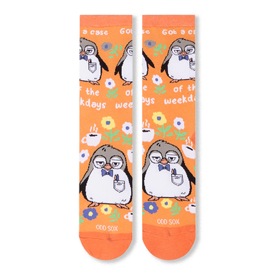 Front flat lay of orange socks showing a repeating pattern of a sleepy penguin, coffee cups, flowers, and white text.
