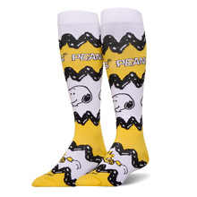Tall yellow and white Peanuts socks featuring Charlie Brown's black zigzag pattern, Snoopy's face, and Woodstock at the toe.