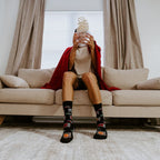 Popcorn tumbles from a glass bowl held up to a man's face on the couch, his planted feet wearing 31 Days of Halloween socks in Black. [lf]