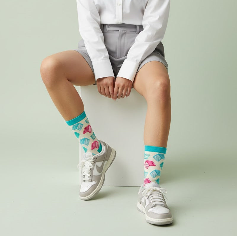 Person seated in white shirt & grey shorts, wearing cream crew socks with teal & pink book pattern & grey sneakers. [lf]