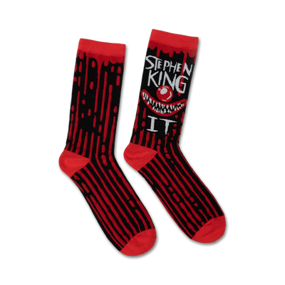 Pair of black and red crew socks.  A grinning Pennywise clown face and 'Stephen King IT' text are featured on one side. Dripping blood design accents the stripes.