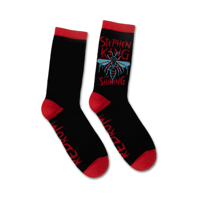 Pair of black crew socks with red cuffs. Features a graphic design of a fly, dripping text that says 'Stephen King The Shining', and 'Redrum' on the sole.