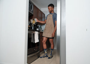 Standing at a stainless oven, an apron-clad home chef pours dry pasta from a paper box into a pot, his Hasta La Pasta socks in Navy planted on the kitchen tile. [lf]