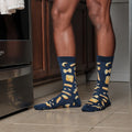 A waist-down kitchen view zooms in on Hasta La Pasta socks in Navy printed with bow-ties, ravioli and farfalle as the wearer stands between dark cabinets and a fridge. [lf]