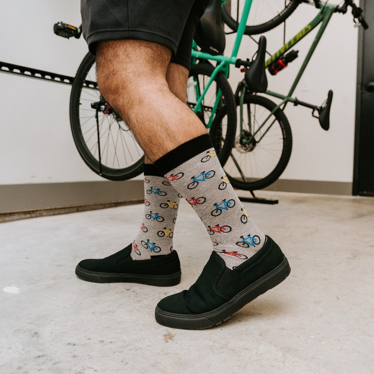 A man caught mid-stride past a green bike on a rack, his Bicyle Race Bamboo socks in Light Gray Heather shown crisply pulled up his calf above black shoes. [lf]
