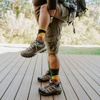 Low-angle piggyback shot highlighting two pairs of Grand Canyon National Park socks in Green Heather above worn-in hiking boots on weathered deck planks. [lf]