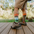 Low-angle calf shot of a man in tan shorts and Merrell hikers, Yellowstone National Park socks in Brown Heather showing the park scene cuff. [lf]
