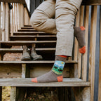 Vertical shot of a person climbing rustic wooden stairs, the bison graphic on Yellowstone National Park socks in Brown Heather front and center. [lf]