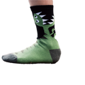Lifestyle shot of a child wearing a pair of green and black T-Rex socks on a tree stump. [lf]
