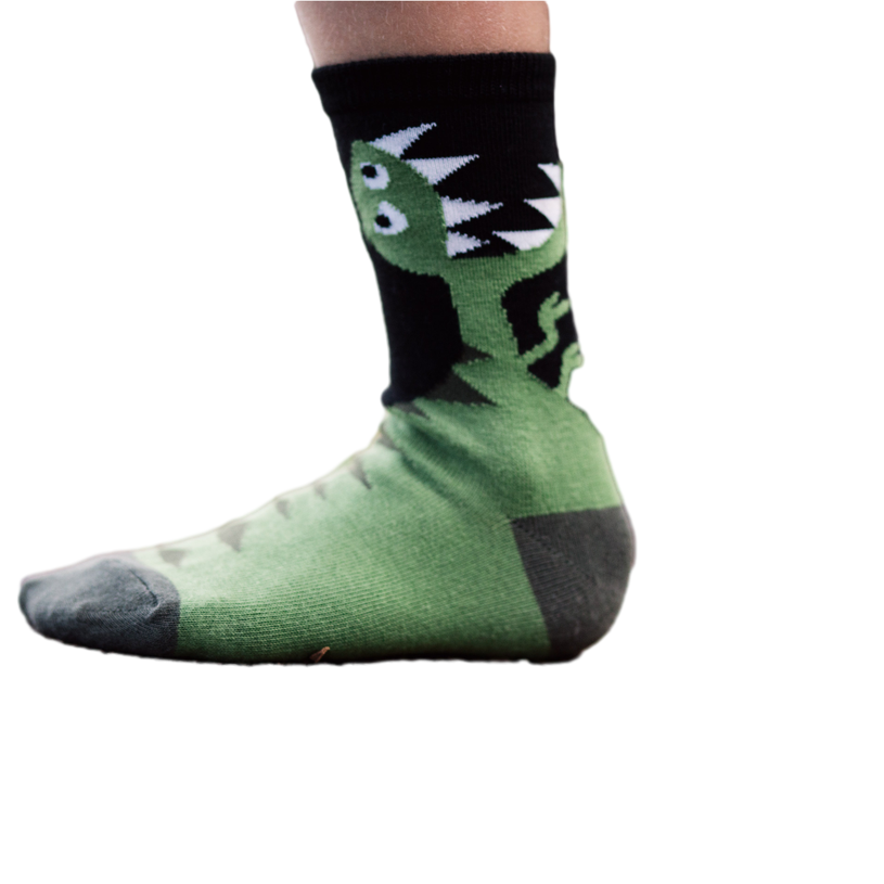 Lifestyle shot of a child wearing a pair of green and black T-Rex socks on a tree stump. [lf]