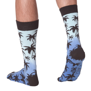 A person is modeling a pair of orange and black palm tree socks. The socks are folded over showing the 