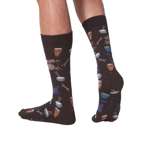 Lifestyle shot showing the 'Drums' socks on a person's legs from the back. The socks are dark brown with a drum set pattern.