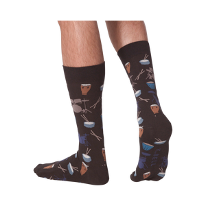 Lifestyle shot showing the 'Drums' socks on a person's legs from the back. The socks are dark brown with a drum set pattern.