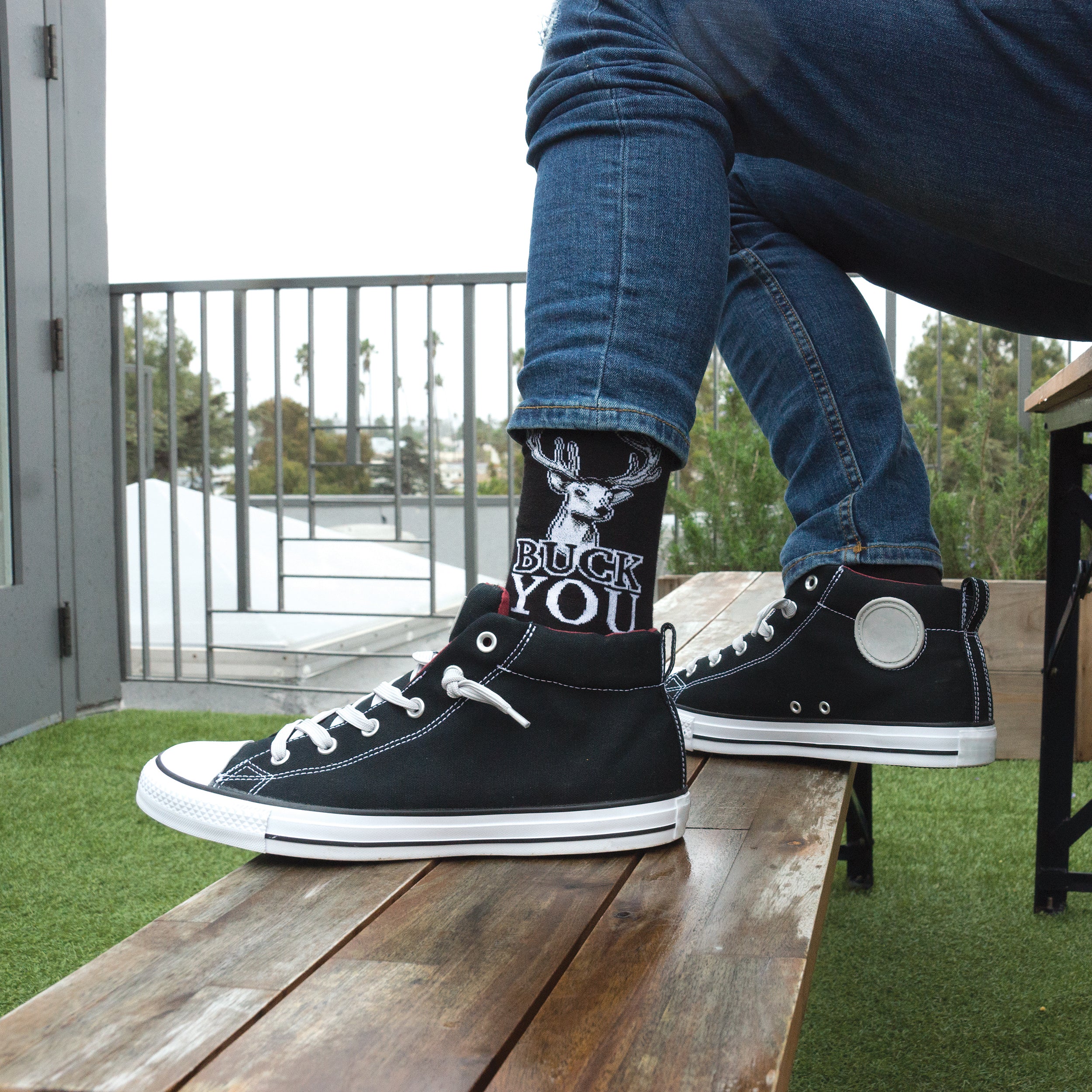 Lifestyle shot: A person wearing 'Buck You' socks and black high-top sneakers. [lf]