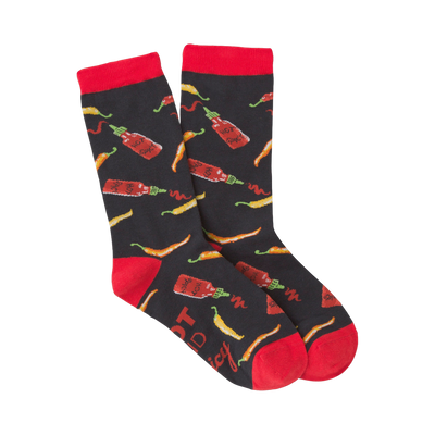 Pair of crew socks with a dark background featuring red and yellow chili peppers and hot sauce bottles.  Red cuffs.