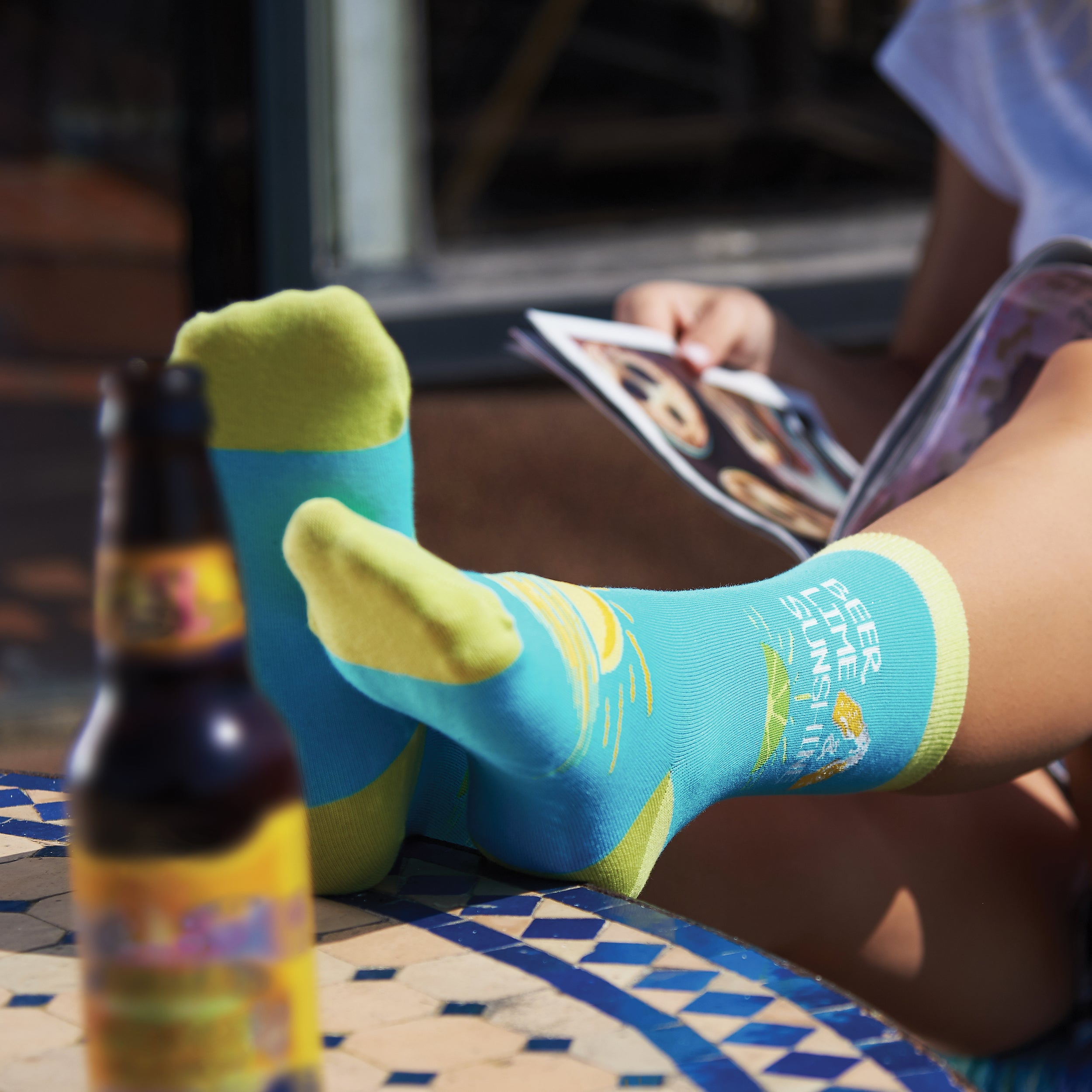 Lifestyle shot of a person relaxing with their feet up, wearing the Beer Lime Sunshine socks.  A beer bottle is visible in the foreground. [lf]