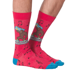 A pair of red socks with a pattern of black musical notes and a cartoonish, blue-footed Bigfoot carrying a boombox on one foot.
