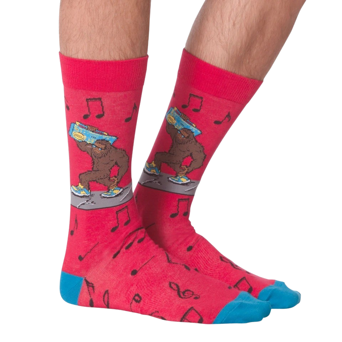 A pair of red socks with a pattern of black musical notes and a cartoonish, blue-footed Bigfoot carrying a boombox on one foot.