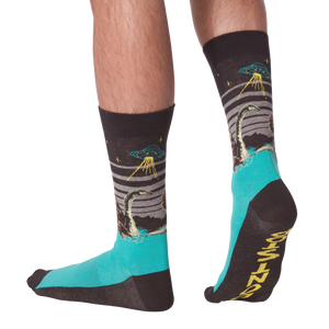 Pair of crew socks worn on legs, showing a dark grey upper with Loch Ness Monster, UFO, and teal feet.