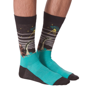Pair of crew socks worn on legs, showing Bigfoot, Loch Ness Monster, and a UFO on a dark grey background with teal feet.