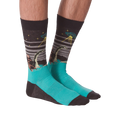 Pair of crew socks worn on legs, showing Bigfoot, Loch Ness Monster, and a UFO on a dark grey background with teal feet.
