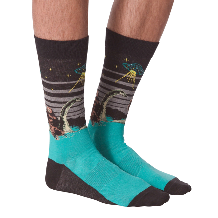 Pair of crew socks worn on legs, showing Bigfoot, Loch Ness Monster, and a UFO on a dark grey background with teal feet.